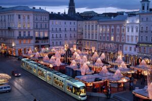 Der winterliche Hauptplatz bietet alljährlich eine wundervolle Kulisse für den Linzer Christkindlmarkt. Die Marktstände sind mit Motiven von Linzer Sehenswürdigkeiten bemalt und symbolisieren mit ihren geschwungenen Vordächern die Wellen des Donaustroms. Foto: Stadt Linz