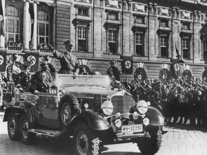 Adolf Hitler erreicht am 15. März 1938 den Wiener Heldenplatz, wo er von Tausenden Österreichern begeistert empfangen und bejubelt wird. Hier vollzog er die Eingliederung des damaligen österreichischen Ständestaates in das Großdeutsche Reich. Neben dem stehenden Hitler im Mercedes sitzend der spätere Bundeskanzler Dr. Arthur Seyss-Inquart. Foto: ÖNB