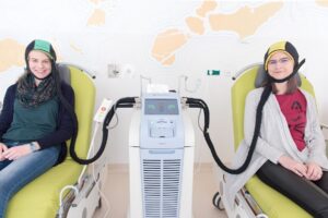 Zwei junge Besucherinnen probieren im St. Josef Krankenhaus Wien aus, wie sich eine Kühlhaube anfühlt. Damit kann der Haarausfall bei einer Chemo reduziert werden. Foto: Peter Rösler